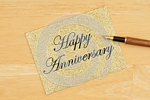 Happy Anniversary greeting card on gold greeting card with pen on textured wood