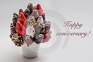 Happy anniversary greeting card with red lettering; A bundle of edible flowers, arrangement of strawberries covered with chocolate