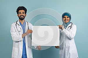 Happy arab doctors in medical uniform and hijab showing blank placard