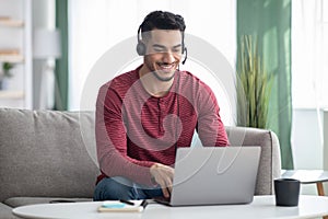 Happy arab guy attending online webinar, using laptop and headset