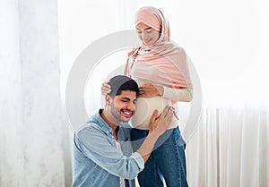 Happy arab man pressing his ear against his wife& x27;s pregnant belly, listening to his baby& x27;s heartbeat, free space