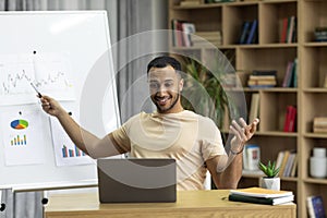 Happy arab man teaching online talking to laptop webcamera, having video call lecture with student, sitting at workplace