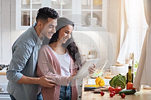 Happy Arab Spouses With Digital Tablet In Kitchen Searching Meal Recipe Online