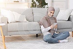 Happy Arab Woman Messaging On Smartphone At Home, Relaxing In Living Room