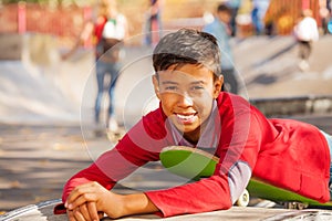 Happy Arabian boy in red shirt lays on skateboard