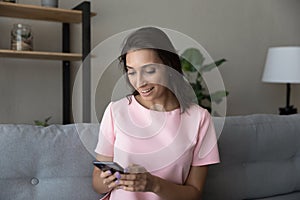 Happy Arabian woman using smartphone, having fun, sitting on couch