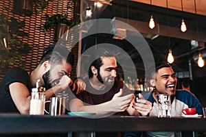 Happy arabian young men hanging in loft cafe. Group of mixed race people having fun in lounge bar