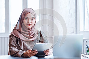 Happy Arabic business woman in brown hijab working with tablet and laptop at office workplace