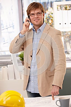 Happy architect talking on phone pointing at table