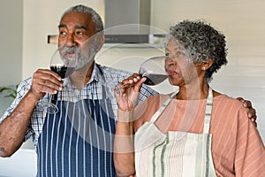 Happy arfican american senior couple drinking wine together in kitchen