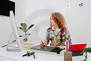 Happy artist woman painting behind work desk on graphics tablet with stylus