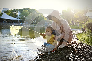 Happy Asia Chinese little boy toddler child play with his mother mom by lake holding string net catch fish carefree childhood