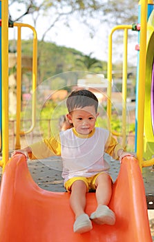 Happy asian baby boy enjoy playing slider in playground in the park