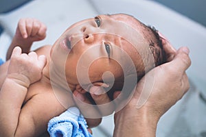 Happy asian baby boy feeling cold to taking bath at the first time of life. mother holding and bathing newborn baby in the morning