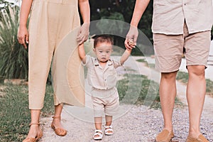 Happy asian baby boy learning to walk first steps with mother and father help at outdoor