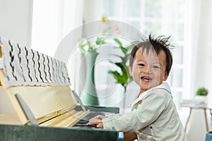 Happy Asian baby toddler smile playing and learning piano at home. Cheerful baby enjoy to develop skills with music. Positive