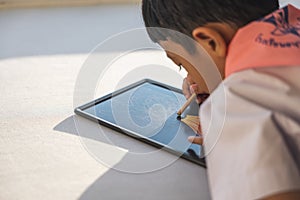 Happy Asian boy 6-7 years old, black hair, white skin, wearing white shirt and blue shorts writing on a chalkboard. Children in