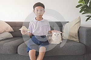 Happy Asian boy 6-7 years old, black-haired, fair-skinned, wearing a white shirt, blue shorts and his British Shorthair cat