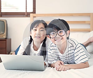Happy asian boy and girl playing game in laptop lying on bed in bedroom in house,brother and sister using notebook do homework,