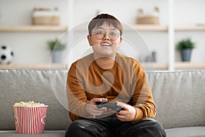 Happy asian boy playing handheld video game at home