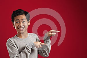 Happy Asian boy surprised smiling to camera while presenting pointing something on his side with copy space