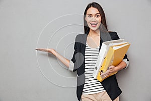 Happy asian business woman with folders holding copyspace on palm