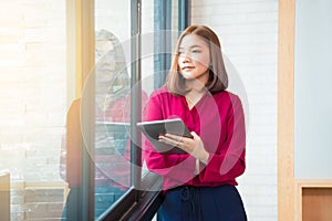 Happy asian business woman standing by large window holding her