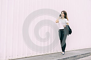 Happy Asian business woman walking and talking smart phone on street in city with white color wall background