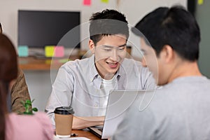 Happy Asian business young man smile and working with laptop and their team in co-working space or modern office