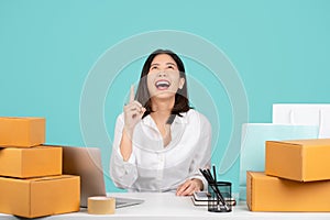 Happy Asian businesswoman with brown cardboard parcel box on white desk  on pastel green background. She looked over and