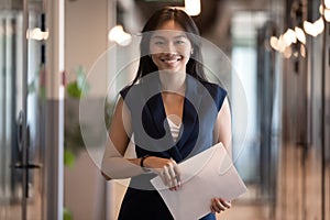 Happy asian businesswoman looking at camera stand in office hallway