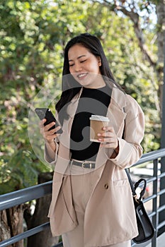 A happy Asian businesswoman is responding to messages on her phone while walking on a skywalk