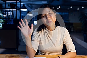 Happy asian businesswoman sitting and waving, making video call, working late at office