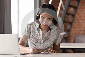 Happy asian businesswoman wearing headset make notes on conference call