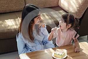 Happy Asian child enjoy eating tasty cake with her older sister