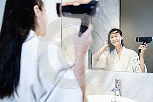 Happy asian child girl drying hair by blowing warm air with hair dryer and looking at the mirror in bathroom,beautiful smiling