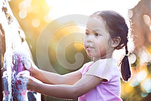 Happy asian child girl having fun to help parent washing car