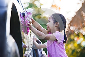 Happy asian child girl having fun to help parent washing car