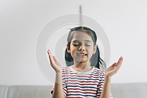 Happy asian child girl meditating at home. Kid sitting on sofa in living room and smiling