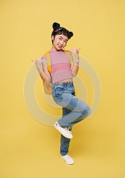 Happy Asian child girl pointing fingers up on yellow background