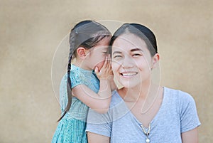 Happy Asian child girl sharing a secret to her mom. Kid girl whispering gossip a something to mother ear