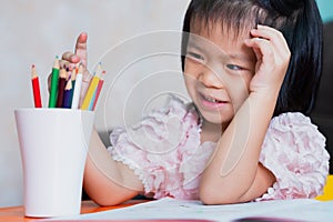 Happy Asian child girl sweet smiling. Kid choosing a wooden crayon. Learning at home. Children aged 4-5 years old