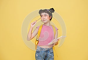 Happy Asian child student holding notebook and pencil with schoolbag isolated on yellow background. idea thinking and creative