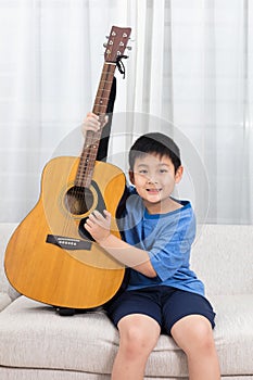 Happy Asian Chinese little boy playing guitar on the sofa