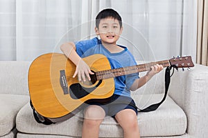 Happy Asian Chinese little boy playing guitar on the sofa