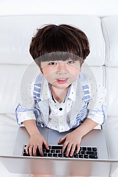 Happy Asian Chinese little boy sitting on couch with laptop