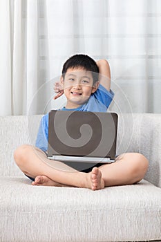 Happy Asian Chinese little boy using laptop on the sofa