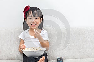 Happy Asian Chinese little girl eating popcorn on the sofa