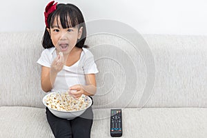 Happy Asian Chinese little girl eating popcorn on the sofa