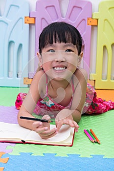 Happy Asian Chinese little girl laying on the floor coloring